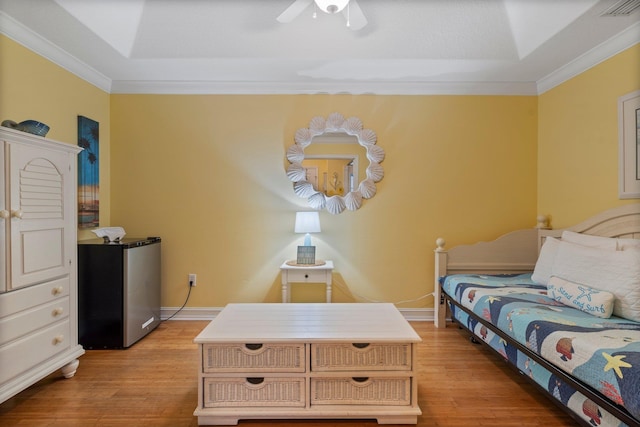 bedroom with light hardwood / wood-style floors, a raised ceiling, stainless steel refrigerator, ceiling fan, and crown molding