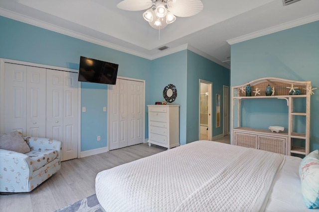 bedroom with light hardwood / wood-style floors, ornamental molding, ceiling fan, a tray ceiling, and multiple closets