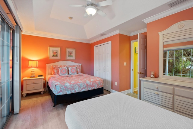 bedroom with ceiling fan, a tray ceiling, a closet, ornamental molding, and light hardwood / wood-style flooring