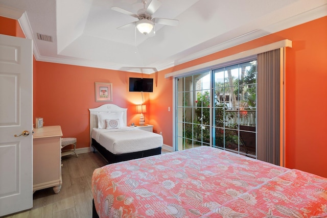 bedroom with ceiling fan, access to outside, a tray ceiling, hardwood / wood-style flooring, and ornamental molding