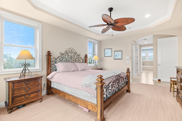 bedroom with multiple windows, a tray ceiling, ensuite bath, and ceiling fan