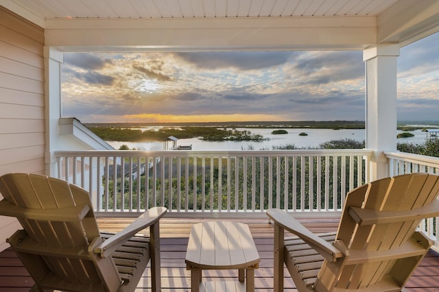 balcony at dusk featuring a water view