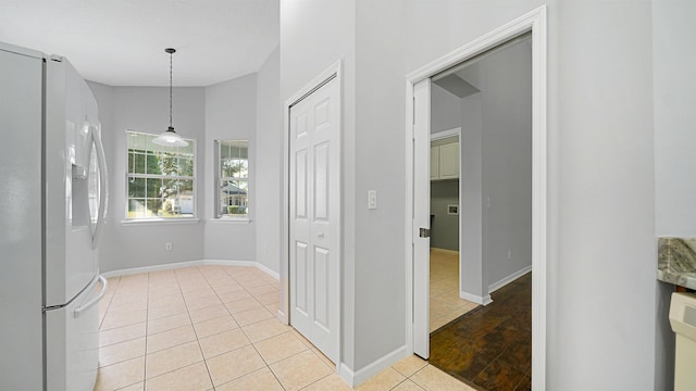 interior space featuring white refrigerator with ice dispenser, light tile patterned flooring, and pendant lighting