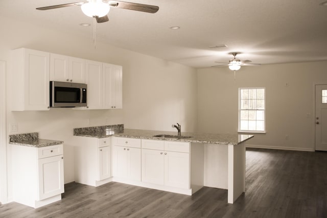 kitchen with white cabinetry, sink, light stone counters, dark hardwood / wood-style flooring, and kitchen peninsula