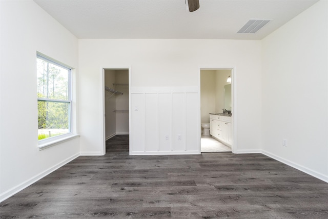 unfurnished bedroom featuring ensuite bathroom, a spacious closet, dark wood-type flooring, and multiple windows