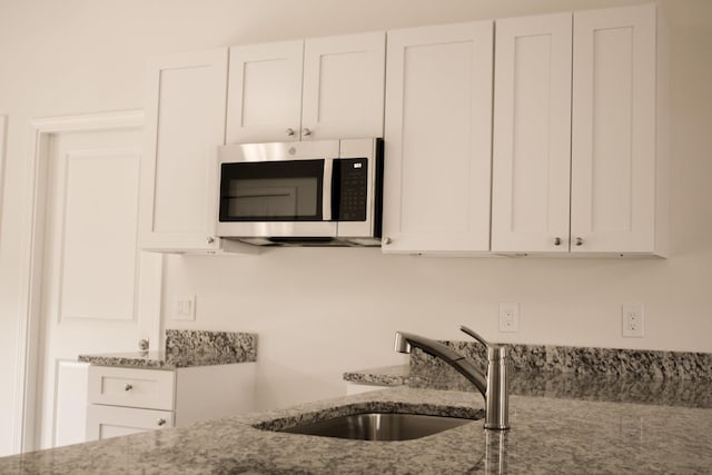 kitchen with white cabinets, light stone counters, and sink