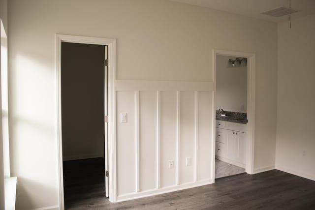 unfurnished bedroom with ensuite bathroom, sink, a spacious closet, and dark hardwood / wood-style floors