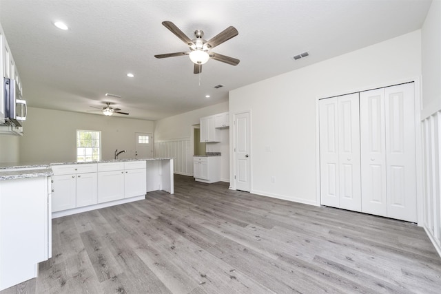 unfurnished living room with a textured ceiling, light wood-type flooring, ceiling fan, and sink