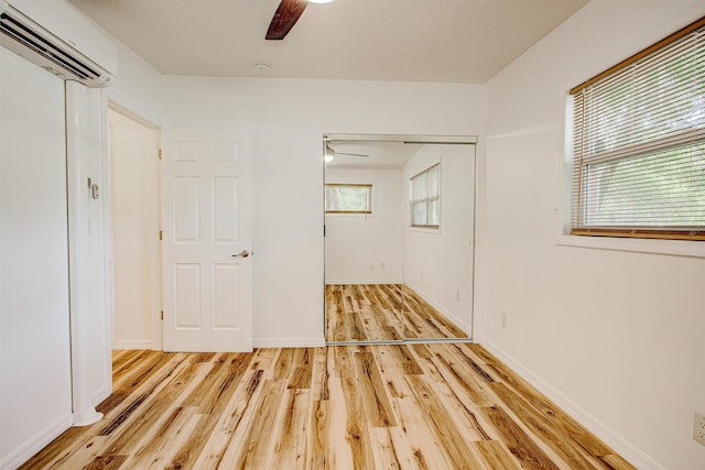 unfurnished bedroom featuring a ceiling fan, multiple windows, wood finished floors, and a wall unit AC