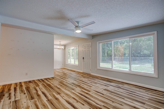 unfurnished room with light wood finished floors, baseboards, lofted ceiling with beams, a textured ceiling, and ceiling fan with notable chandelier