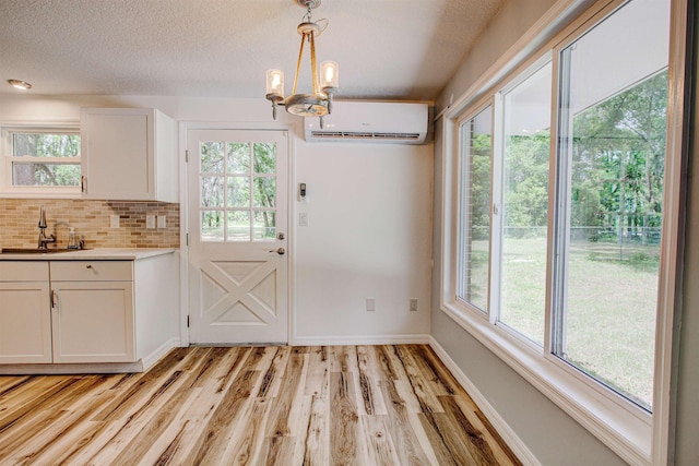 unfurnished dining area featuring a wall mounted air conditioner, light wood finished floors, a sink, baseboards, and a chandelier