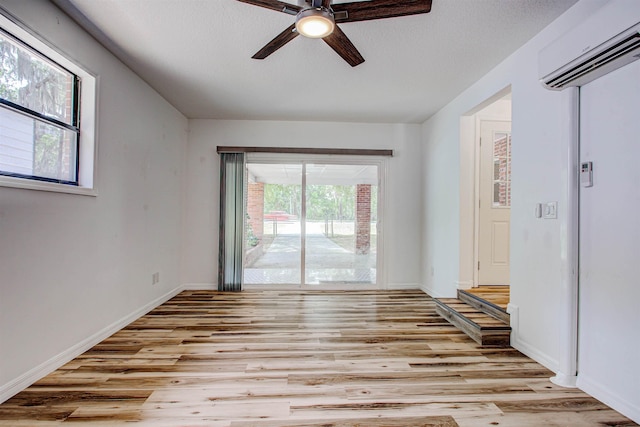 unfurnished room featuring a wall mounted air conditioner, baseboards, a ceiling fan, and light wood-style flooring
