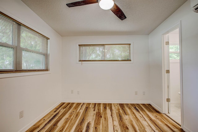 empty room with a wall mounted air conditioner, a textured ceiling, ceiling fan, light wood finished floors, and baseboards