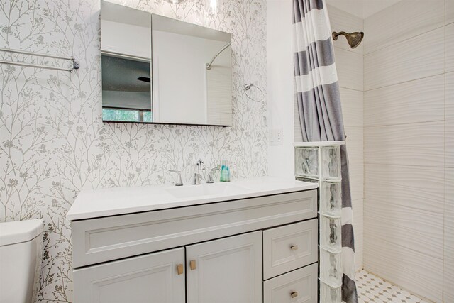 full bathroom with wallpapered walls, toilet, vanity, and a tile shower