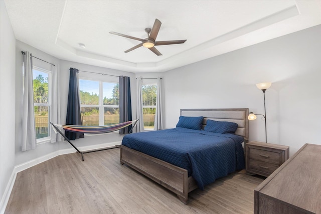 bedroom with ceiling fan, a tray ceiling, and light wood-type flooring