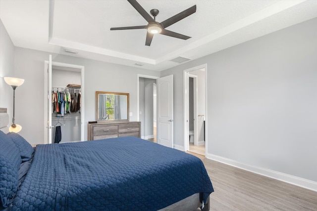 bedroom featuring a raised ceiling, ceiling fan, a spacious closet, and light wood-type flooring