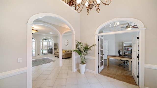 entryway with light tile patterned floors, arched walkways, ceiling fan with notable chandelier, a high ceiling, and baseboards