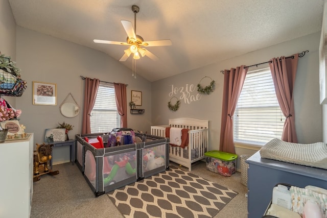 carpeted bedroom featuring ceiling fan, vaulted ceiling, a nursery area, and a textured ceiling