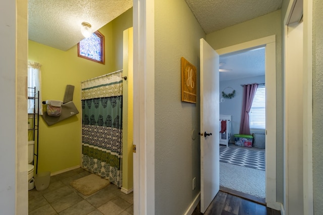 hall featuring light tile flooring, a healthy amount of sunlight, and a textured ceiling