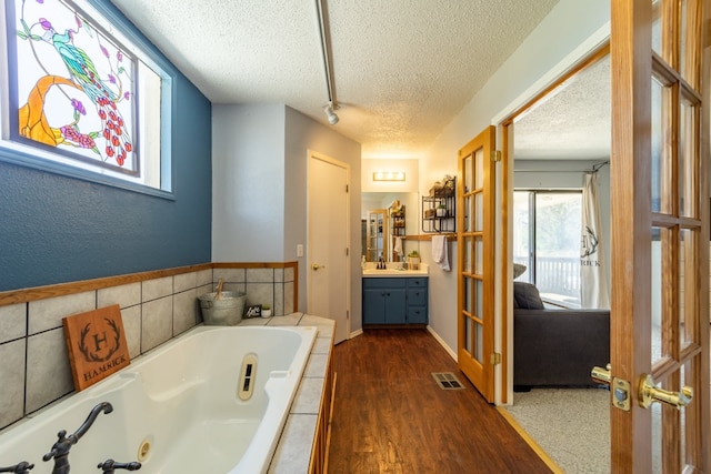 bathroom featuring a relaxing tiled bath, vanity, a textured ceiling, and hardwood / wood-style flooring