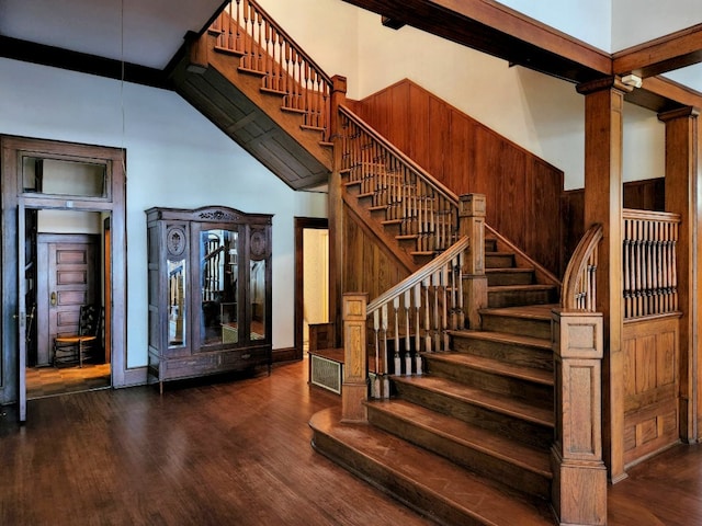 staircase with a high ceiling, beam ceiling, dark hardwood / wood-style floors, and decorative columns