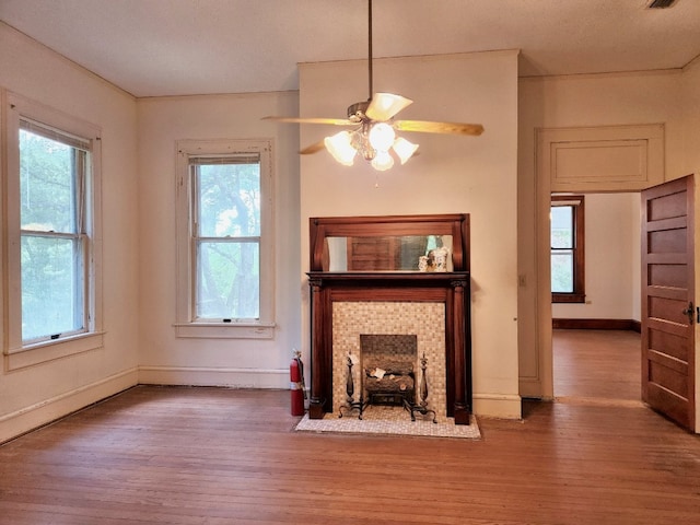 unfurnished living room featuring ceiling fan, a tile fireplace, plenty of natural light, and dark hardwood / wood-style floors