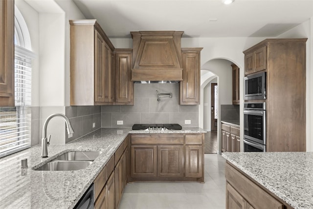 kitchen with appliances with stainless steel finishes, backsplash, custom range hood, light stone counters, and sink