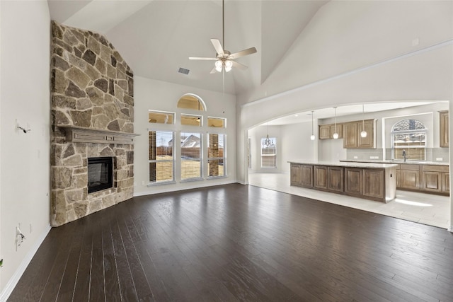 unfurnished living room featuring high vaulted ceiling, a stone fireplace, ceiling fan, dark tile flooring, and sink