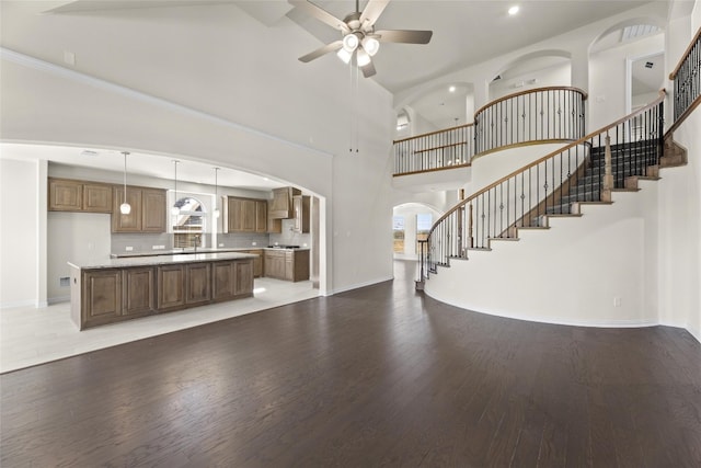 interior space featuring ceiling fan, a center island, wall chimney exhaust hood, wood-type flooring, and pendant lighting