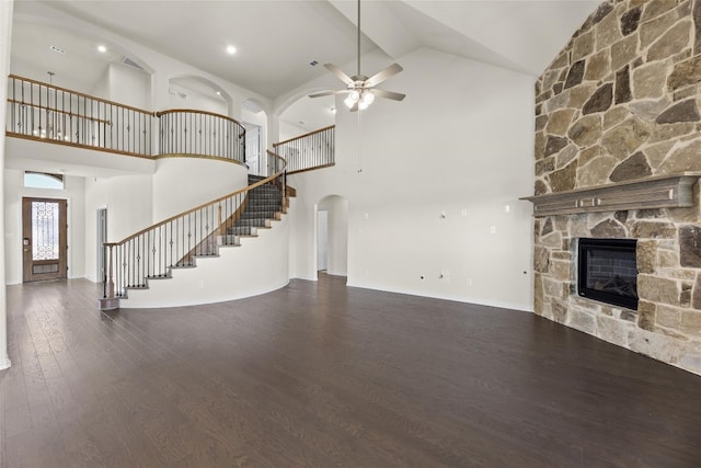 unfurnished living room featuring dark hardwood / wood-style floors, high vaulted ceiling, ceiling fan, and a stone fireplace