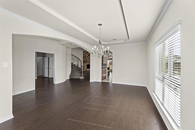 unfurnished room featuring crown molding, dark wood-type flooring, a tray ceiling, a fireplace, and an inviting chandelier