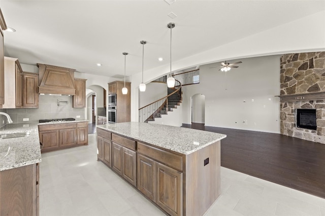 kitchen with a kitchen island, light hardwood / wood-style flooring, ceiling fan, custom range hood, and a fireplace