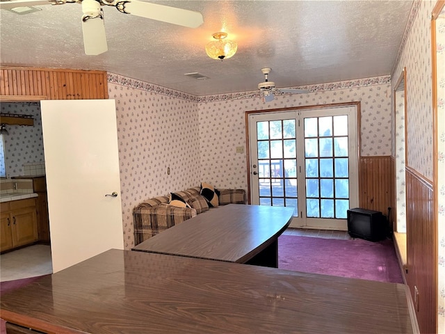 unfurnished dining area with ceiling fan, dark colored carpet, and a textured ceiling