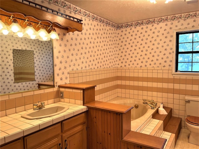 bathroom featuring tile walls, toilet, tiled bath, a textured ceiling, and vanity