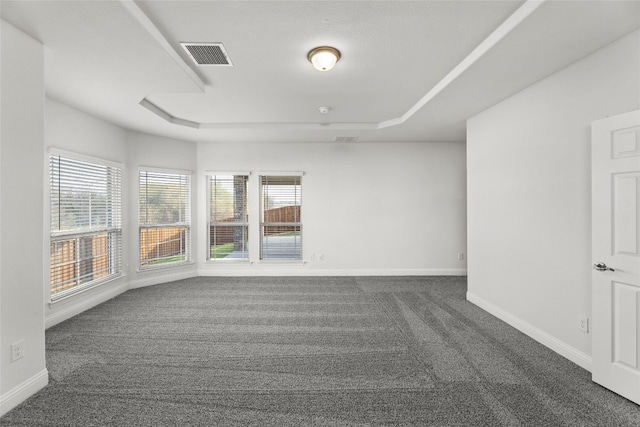 unfurnished room with a tray ceiling and dark colored carpet