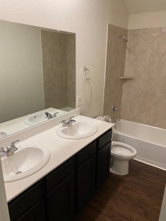 full bathroom with toilet, dual vanity, tiled shower / bath, and wood-type flooring