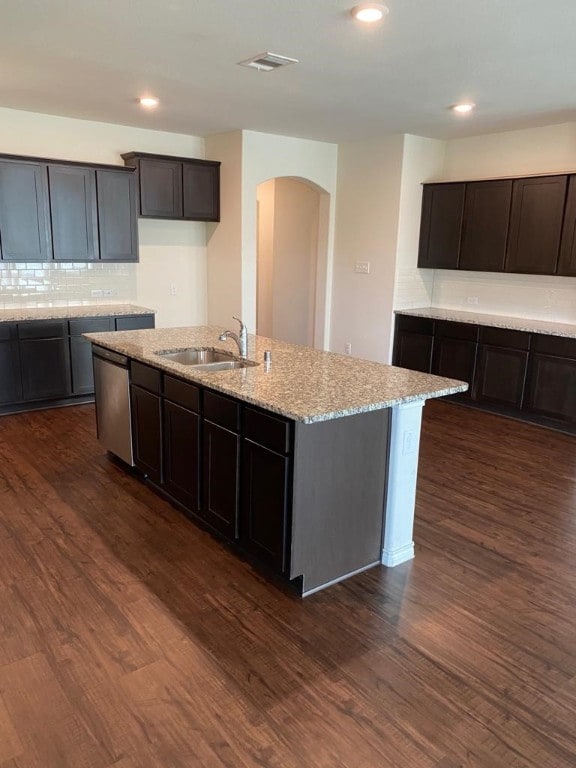 kitchen with an island with sink, sink, dark hardwood / wood-style flooring, light stone countertops, and tasteful backsplash