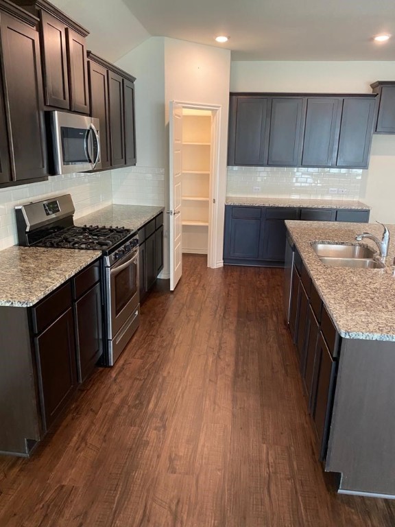 kitchen with dark wood-type flooring, tasteful backsplash, dark brown cabinets, stainless steel appliances, and sink