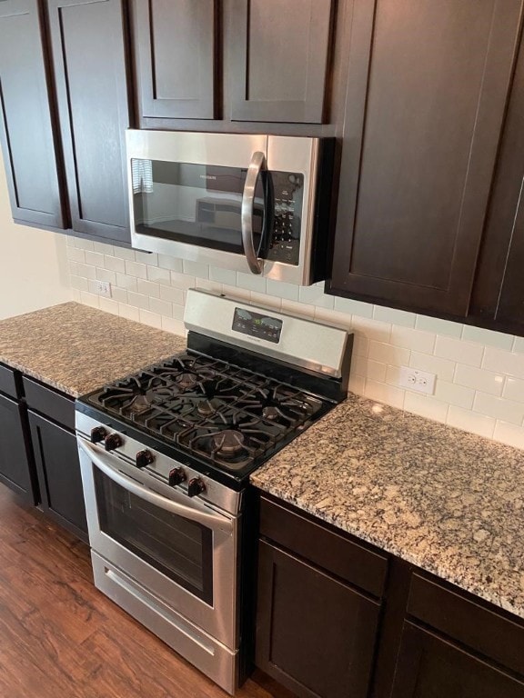 kitchen featuring backsplash, dark hardwood / wood-style floors, stainless steel appliances, and light stone countertops