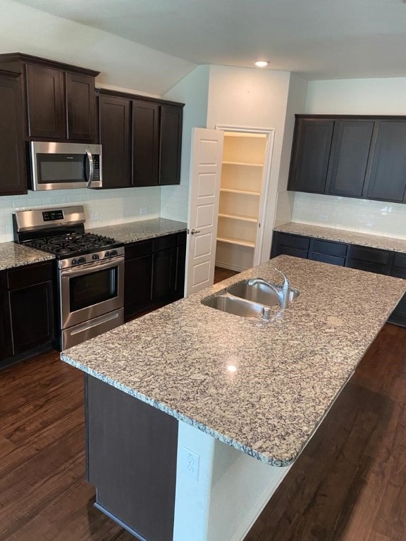 kitchen featuring dark wood-type flooring, light stone counters, an island with sink, stainless steel appliances, and sink