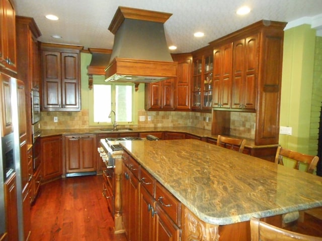 kitchen with sink, light stone counters, a breakfast bar, custom range hood, and stainless steel oven