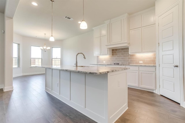 kitchen featuring white cabinets, a center island with sink, sink, backsplash, and hanging light fixtures