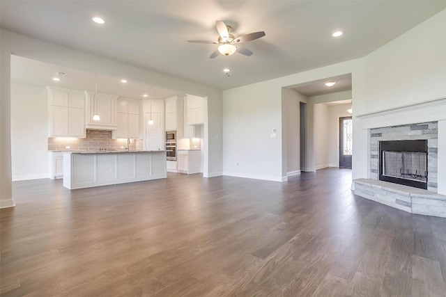 unfurnished living room featuring a fireplace, ceiling fan, sink, and dark hardwood / wood-style flooring