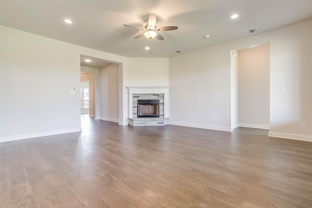 unfurnished living room featuring ceiling fan, a stone fireplace, and dark wood-type flooring