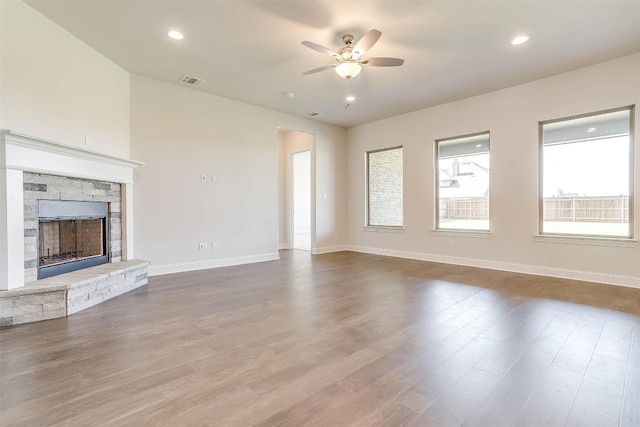 unfurnished living room featuring ceiling fan, a stone fireplace, and dark wood-type flooring