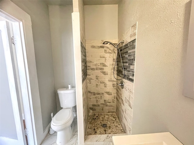 bathroom with toilet, tiled shower, and tile floors