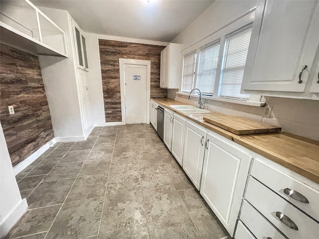 kitchen with wood walls, white cabinetry, light tile floors, dishwasher, and sink