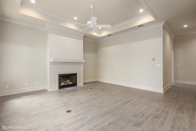 unfurnished living room featuring a large fireplace, a tray ceiling, ceiling fan, and light wood-type flooring