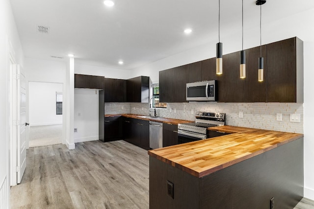 kitchen featuring pendant lighting, butcher block countertops, stainless steel appliances, light hardwood / wood-style flooring, and backsplash