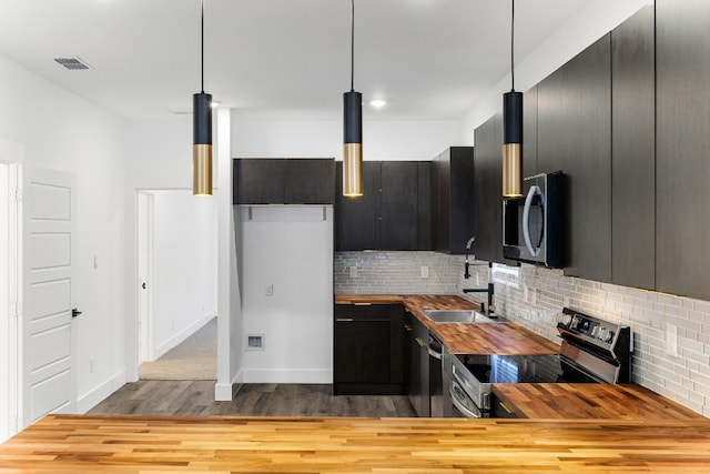 kitchen with butcher block countertops, stainless steel appliances, decorative light fixtures, and tasteful backsplash